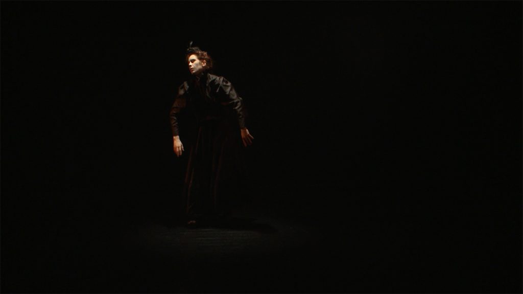 Video still from artwork where artist Maria Norrman interprets and invokes dance artist Jane Avril.
The artist in a dancing pose, dressed in black 19th century clothing.