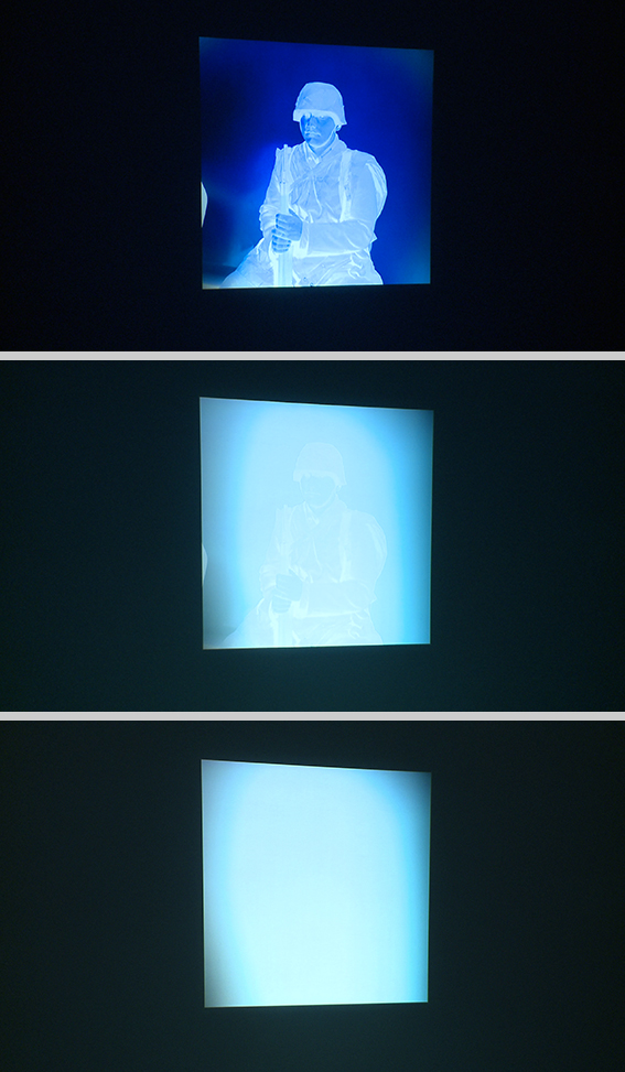 The video projection Blue Prints. Images of an inverted analogue negative of a seated man in a uniform, which fades from visible to white.